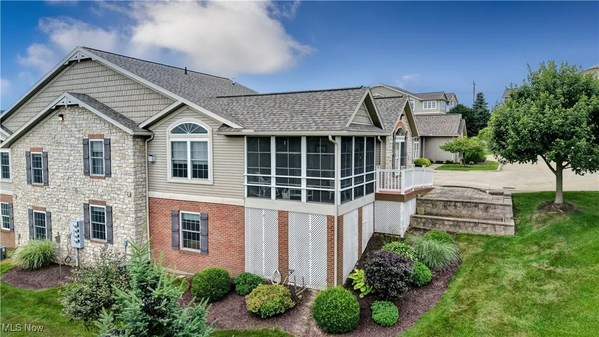 View of home's exterior with a sunroom, brick siding, stone siding, roof with shingles, and a lawn