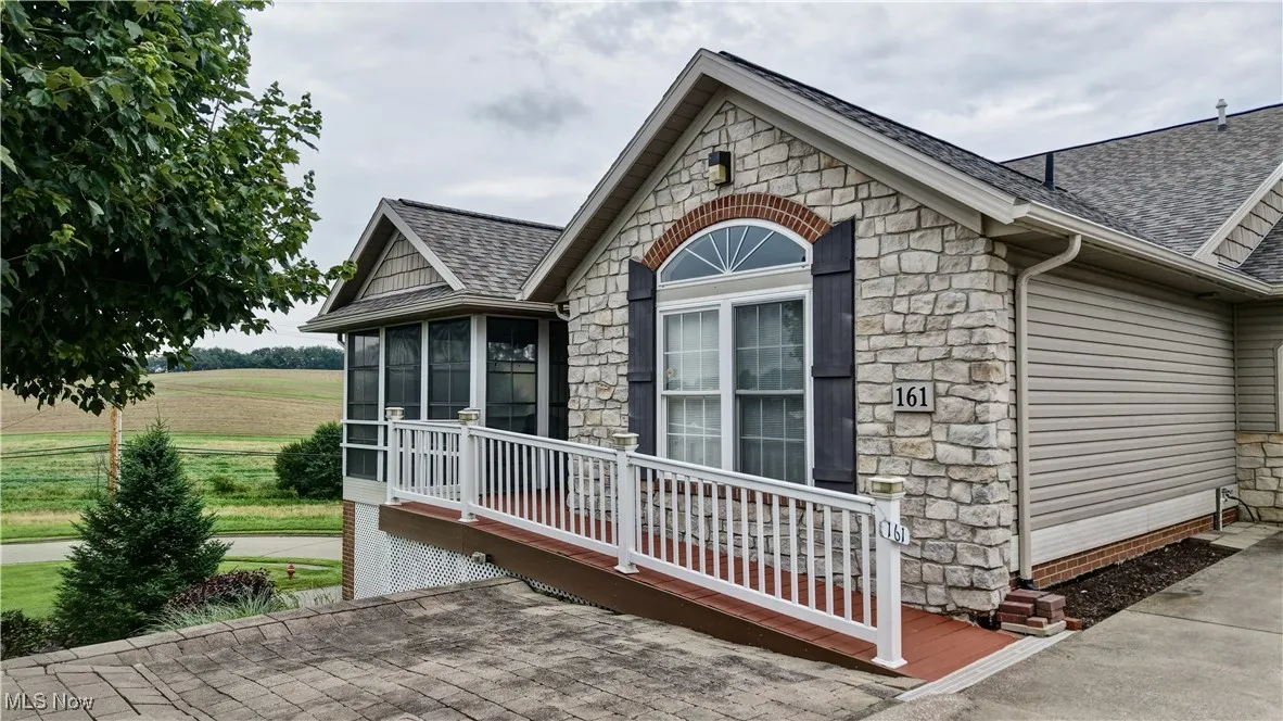 View of side of property featuring roof with shingles, stone siding, and a sunroom