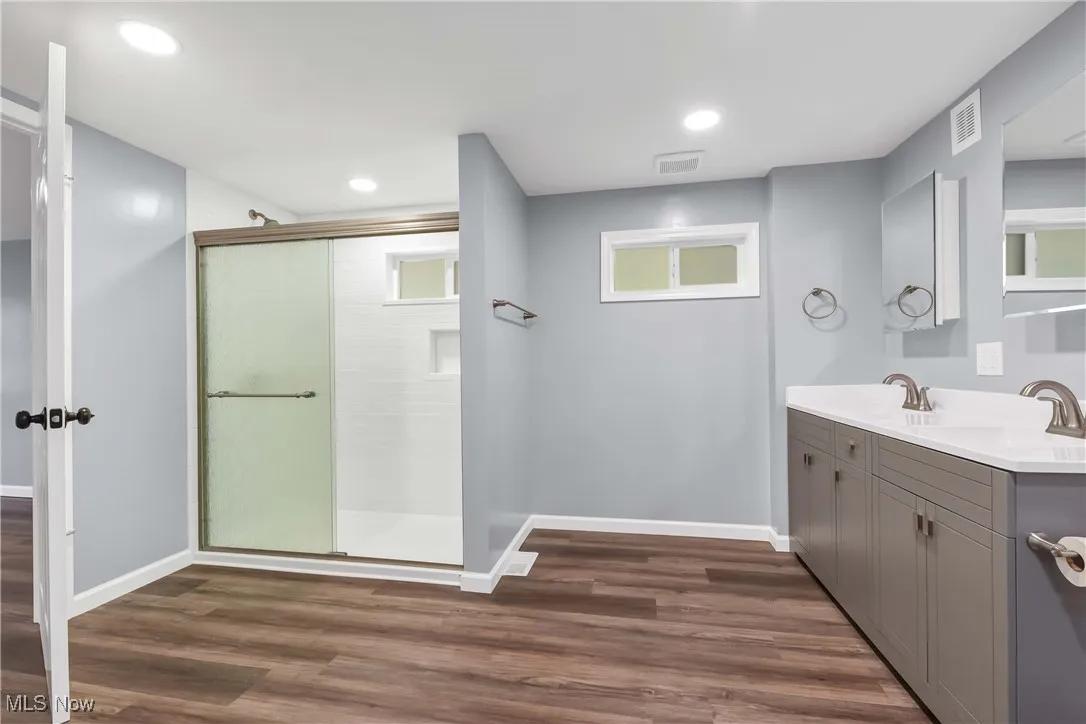 Full bath with a stall shower, double vanity, wood finished floors, and recessed lighting