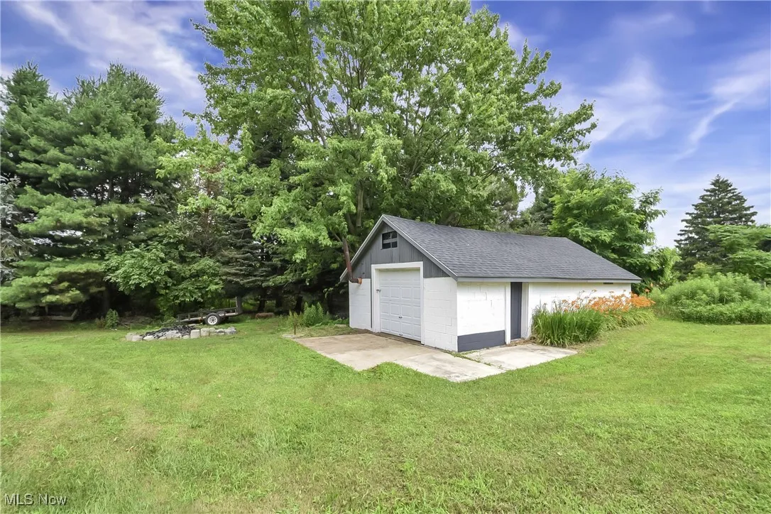 View of green lawn featuring a detached garage, an outbuilding, and driveway