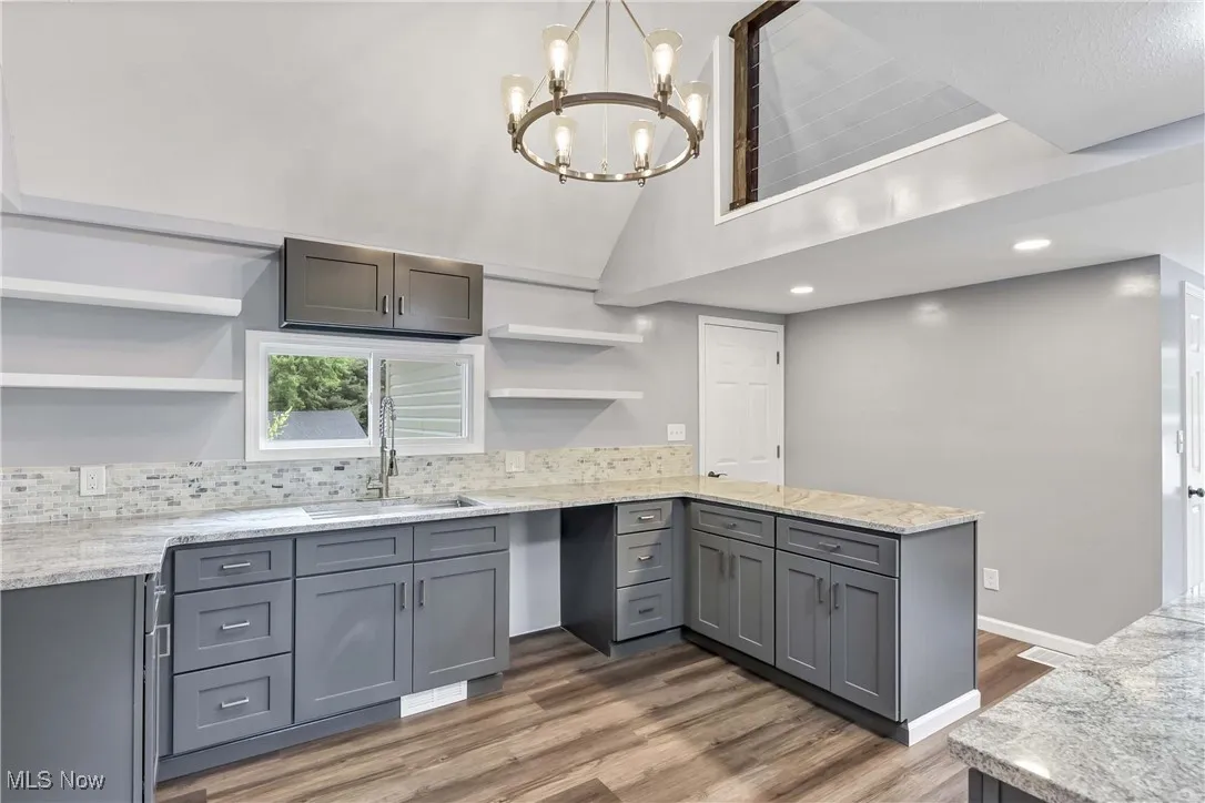 Kitchen with open shelves, a peninsula, gray cabinetry, light wood-style flooring, and a chandelier