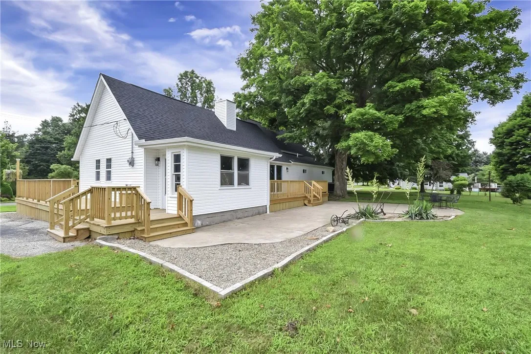 Back of house featuring roof with shingles, a patio, a wooden deck, and a chimney