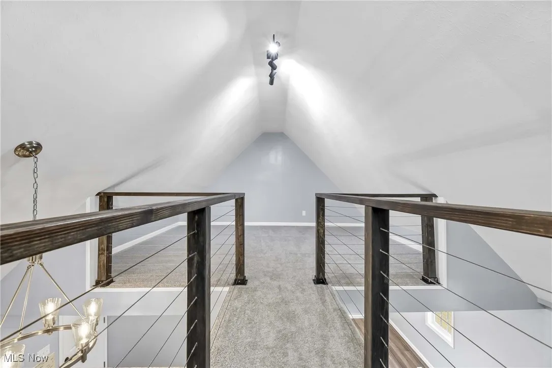 Hall featuring lofted ceiling, carpet, an upstairs landing, and a chandelier