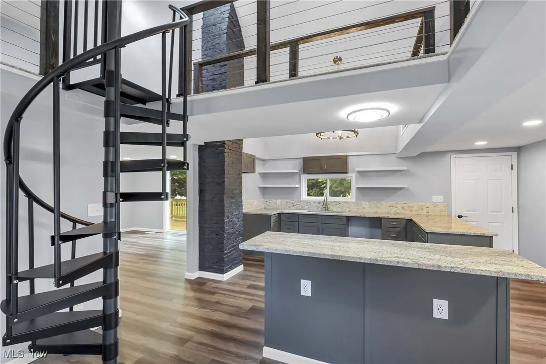 Kitchen featuring open shelves, dark wood-style flooring, a towering ceiling, gray cabinets, and light stone counters