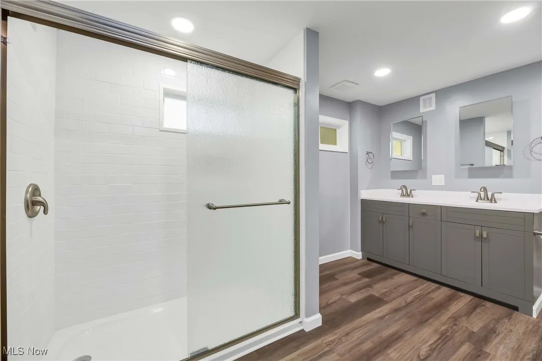 Full bathroom with a stall shower, double vanity, wood finished floors, and recessed lighting