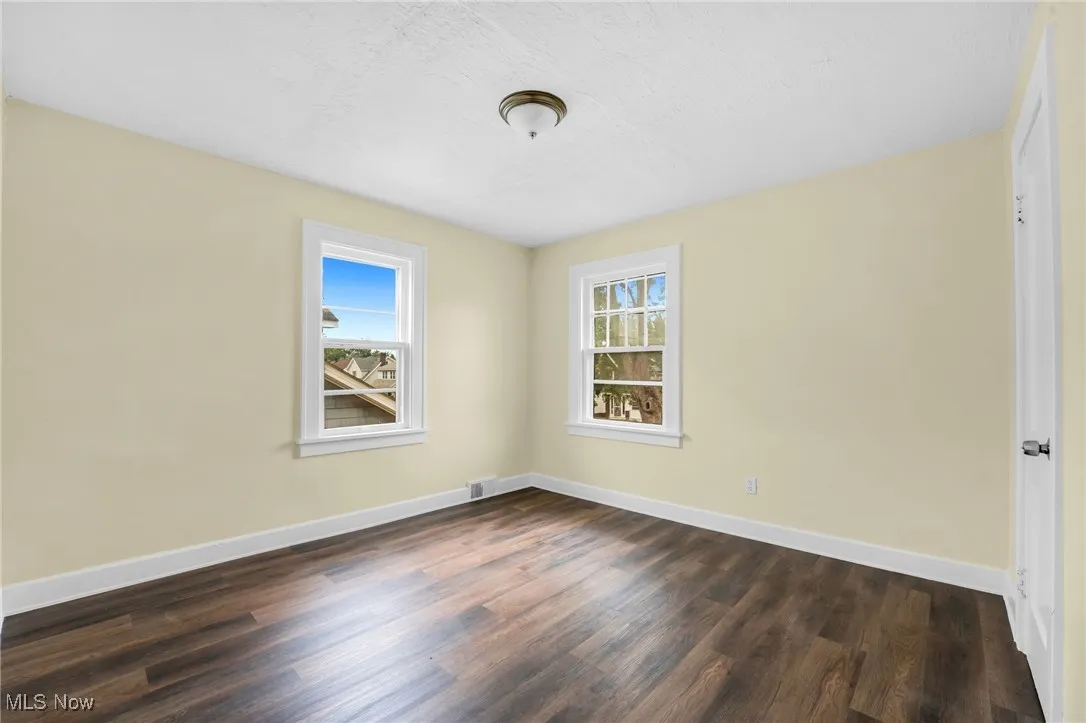 Unfurnished room with dark wood-style floors and healthy amount of natural light