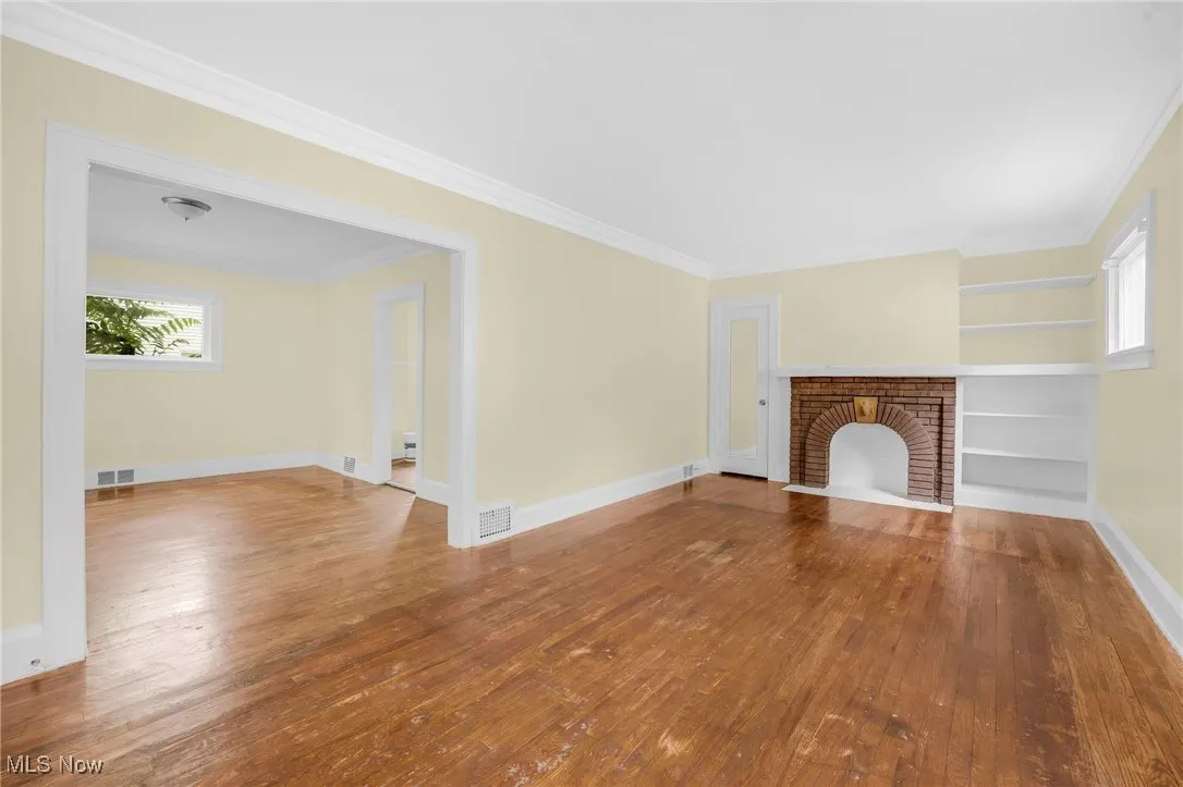 Unfurnished living room with hardwood / wood-style flooring, plenty of natural light, a fireplace, and ornamental molding