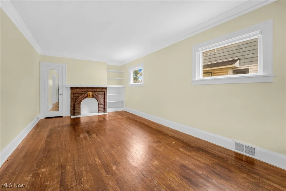 Unfurnished living room featuring wood-type flooring, a fireplace, crown molding, and built in shelves