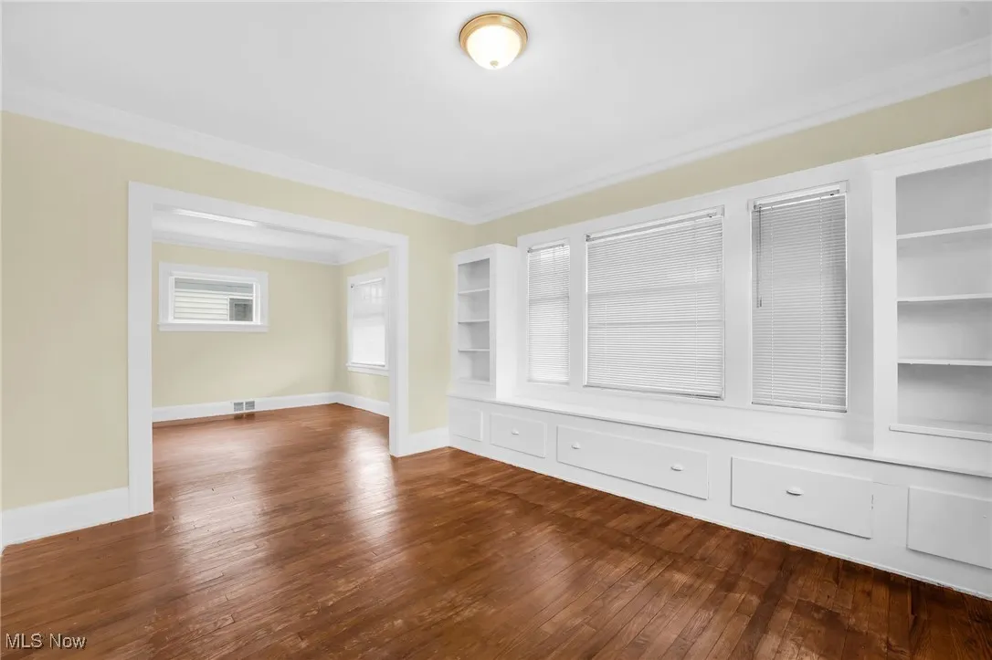 Unfurnished room with crown molding, dark wood finished floors, and built in shelves