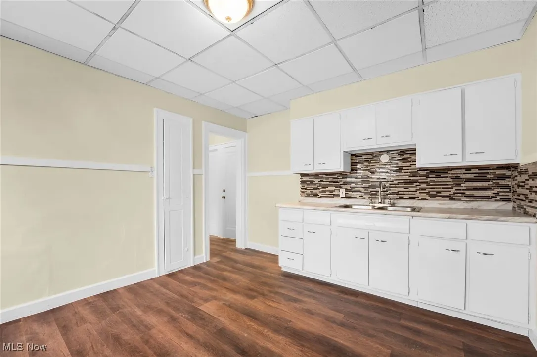 Kitchen featuring a paneled ceiling, light countertops, backsplash, dark wood finished floors, and white cabinets