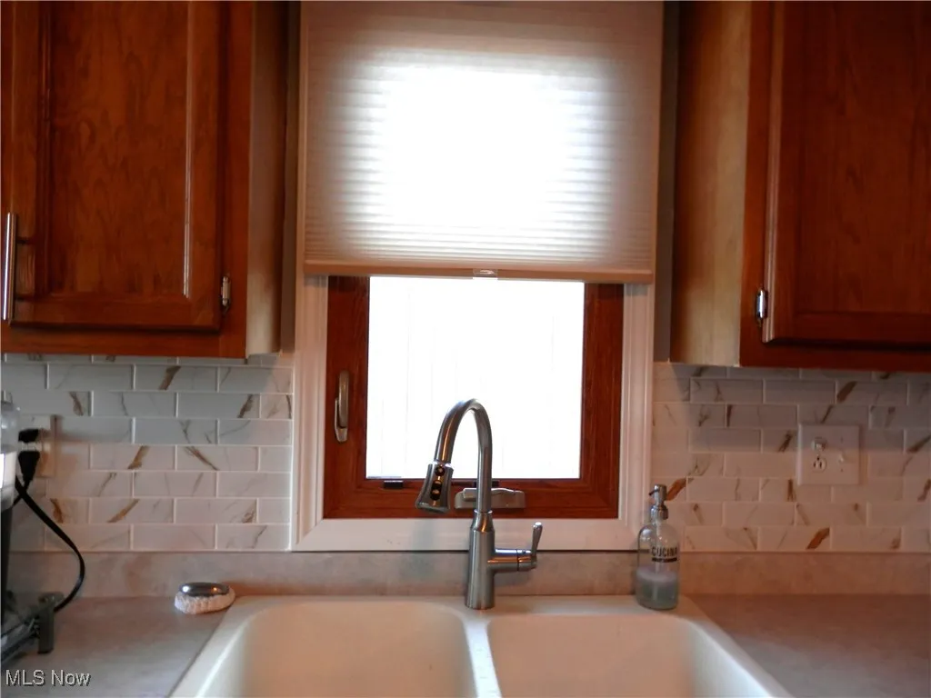 Kitchen with light countertops, decorative backsplash, and brown cabinets