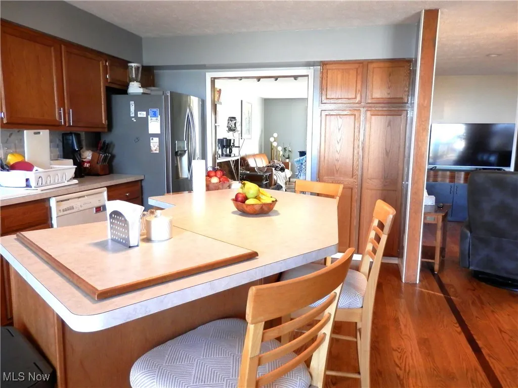 Kitchen featuring stainless steel fridge, light countertops, wood finished floors, white dishwasher, and brown cabinetry