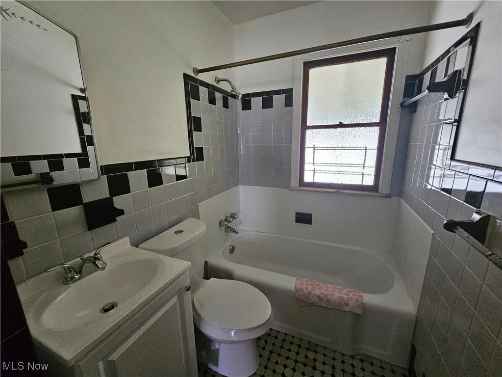 Bathroom with tile walls, tub / shower combination, and vanity