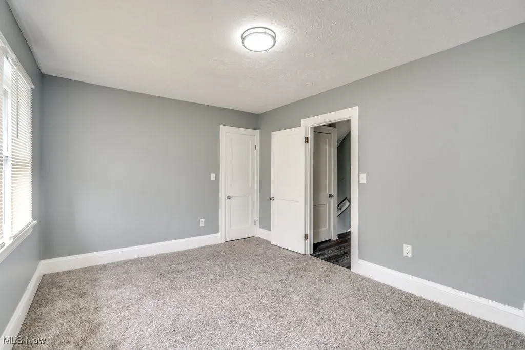 Unfurnished bedroom featuring dark colored carpet, multiple windows, and a textured ceiling