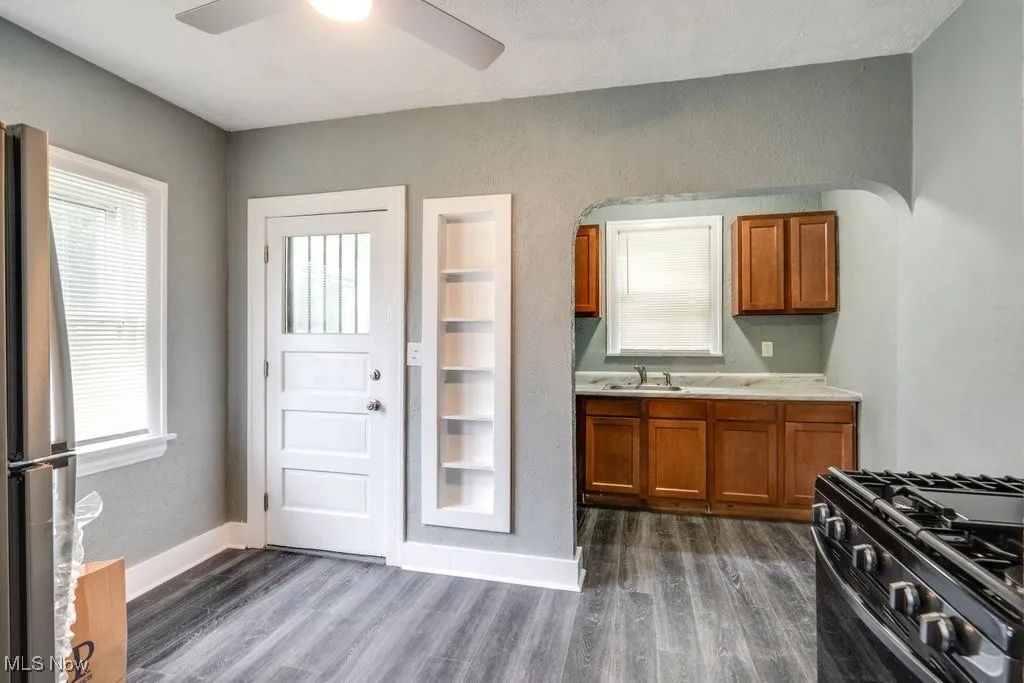 Kitchen featuring brown cabinets, freestanding refrigerator, gas stove, a ceiling fan, and dark wood-type flooring