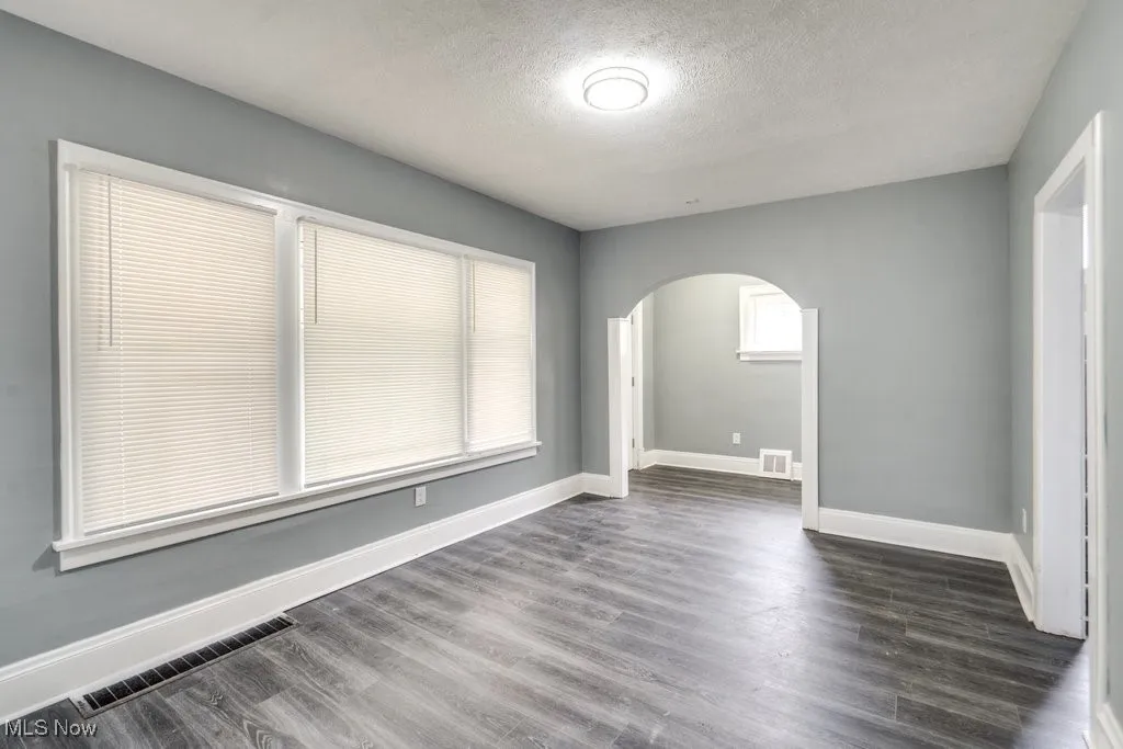 Unfurnished room with arched walkways, a textured ceiling, and dark wood-type flooring