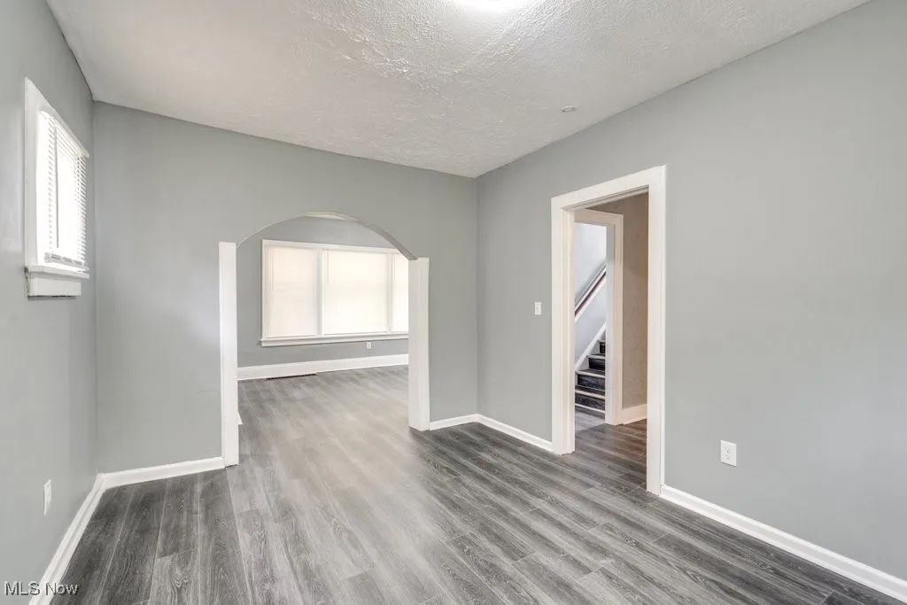 Empty room featuring arched walkways, wood finished floors, a textured ceiling, and stairs