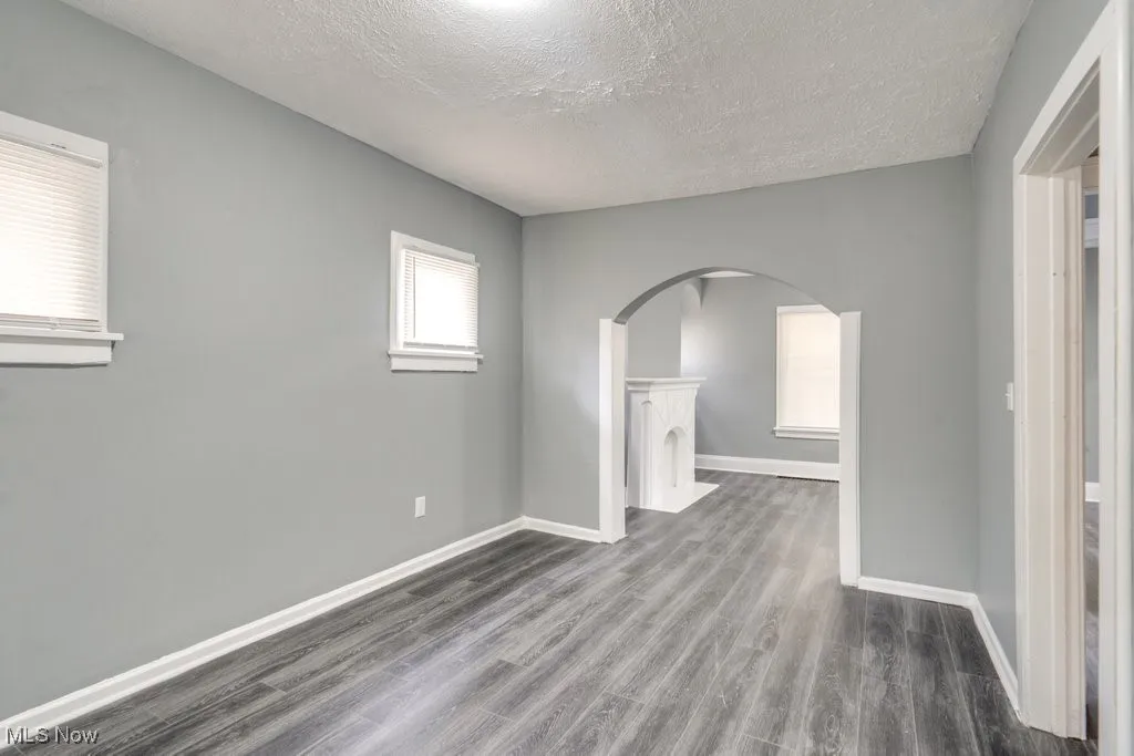 Unfurnished room with arched walkways, a textured ceiling, and wood finished floors