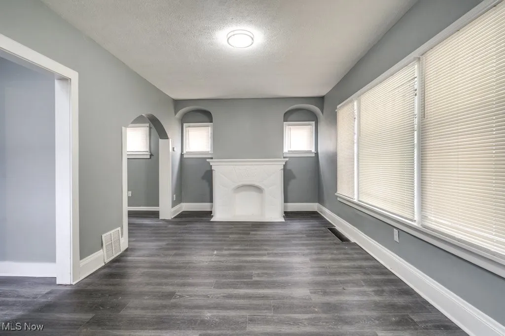 Unfurnished living room with a textured ceiling, arched walkways, and dark wood finished floors