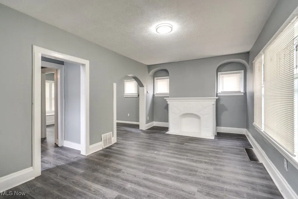 Unfurnished living room with a textured ceiling, arched walkways, and dark wood finished floors