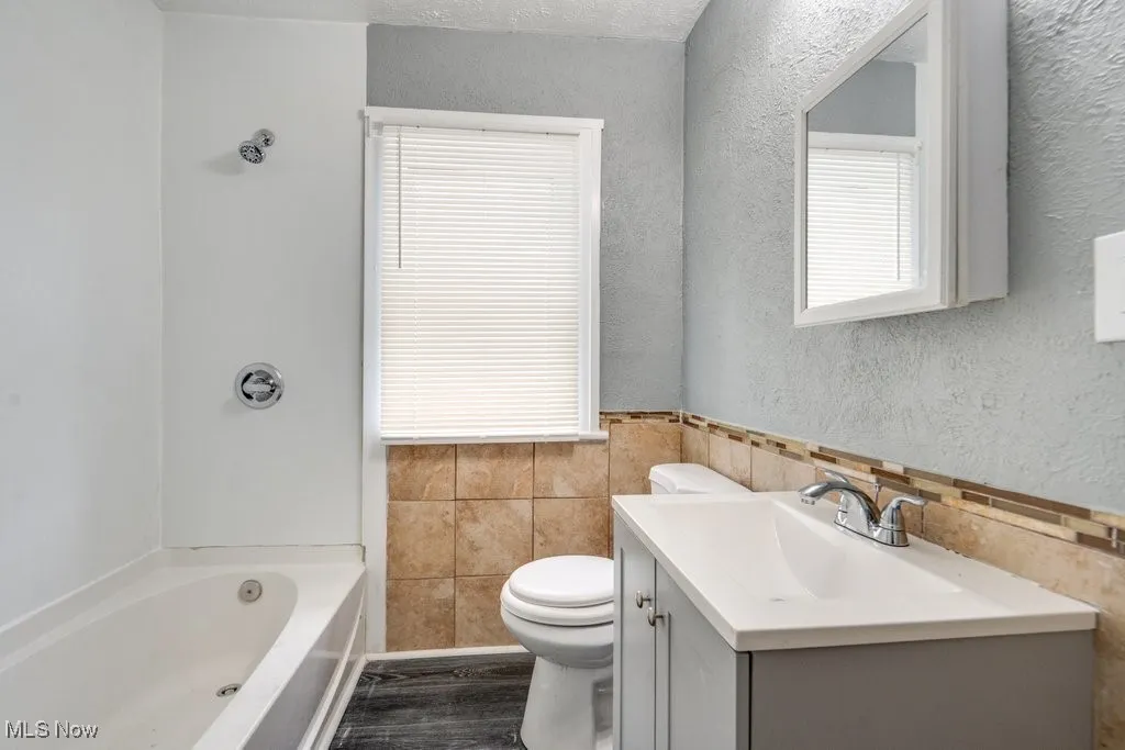 Bathroom with tile walls, vanity, wood finished floors, a textured wall, and bathing tub / shower combination