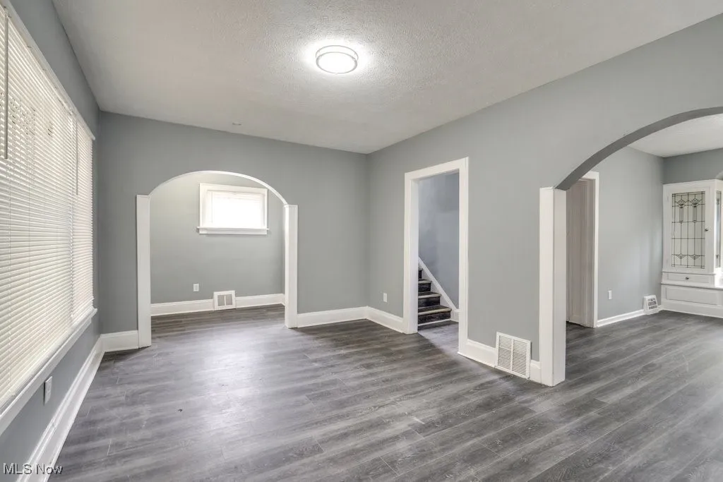 Empty room featuring arched walkways, a textured ceiling, dark wood-style floors, and stairway