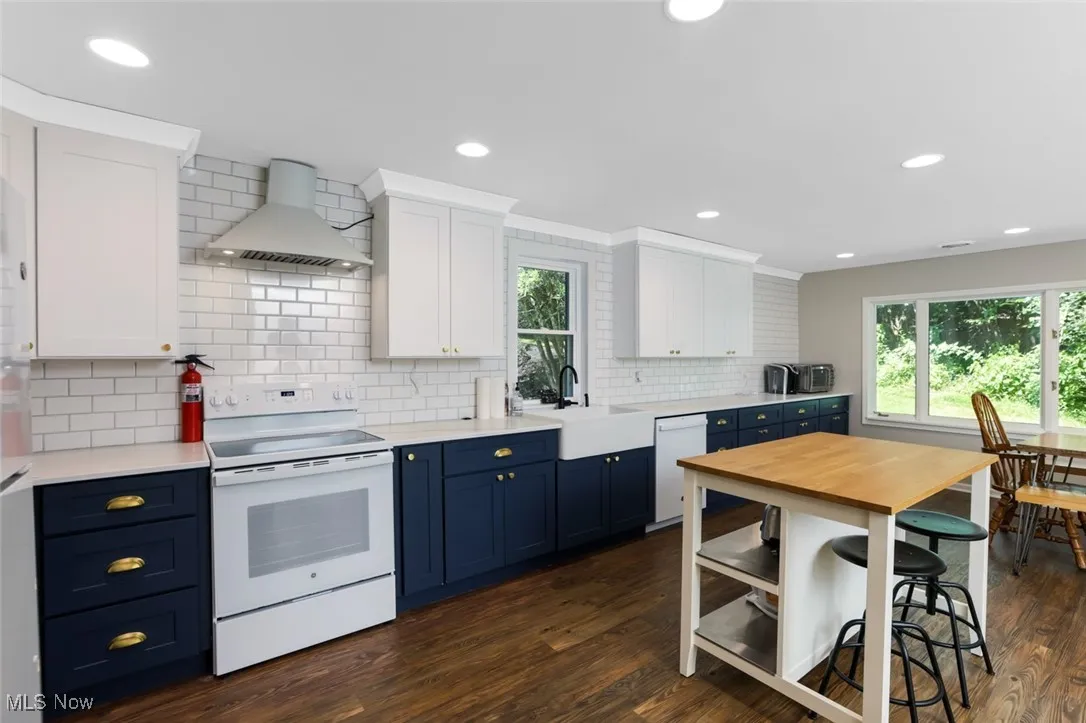 Kitchen with white appliances, blue cabinetry, dark wood-style flooring, white cabinetry, and recessed lighting