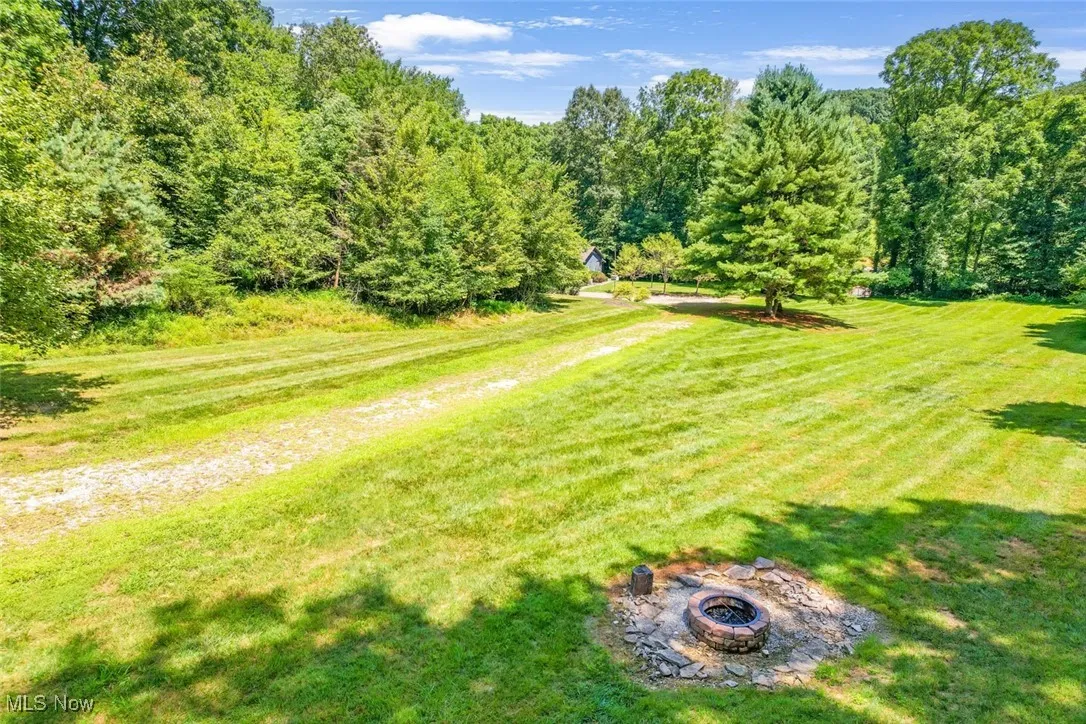 View of green lawn featuring an outdoor fire pit and a forest view