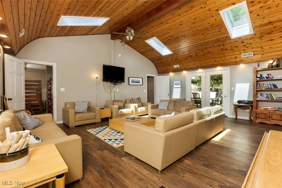 Living room with a skylight, a wooden ceiling with exposed beams, dark wood finished floors, high vaulted ceiling, and ceiling fan