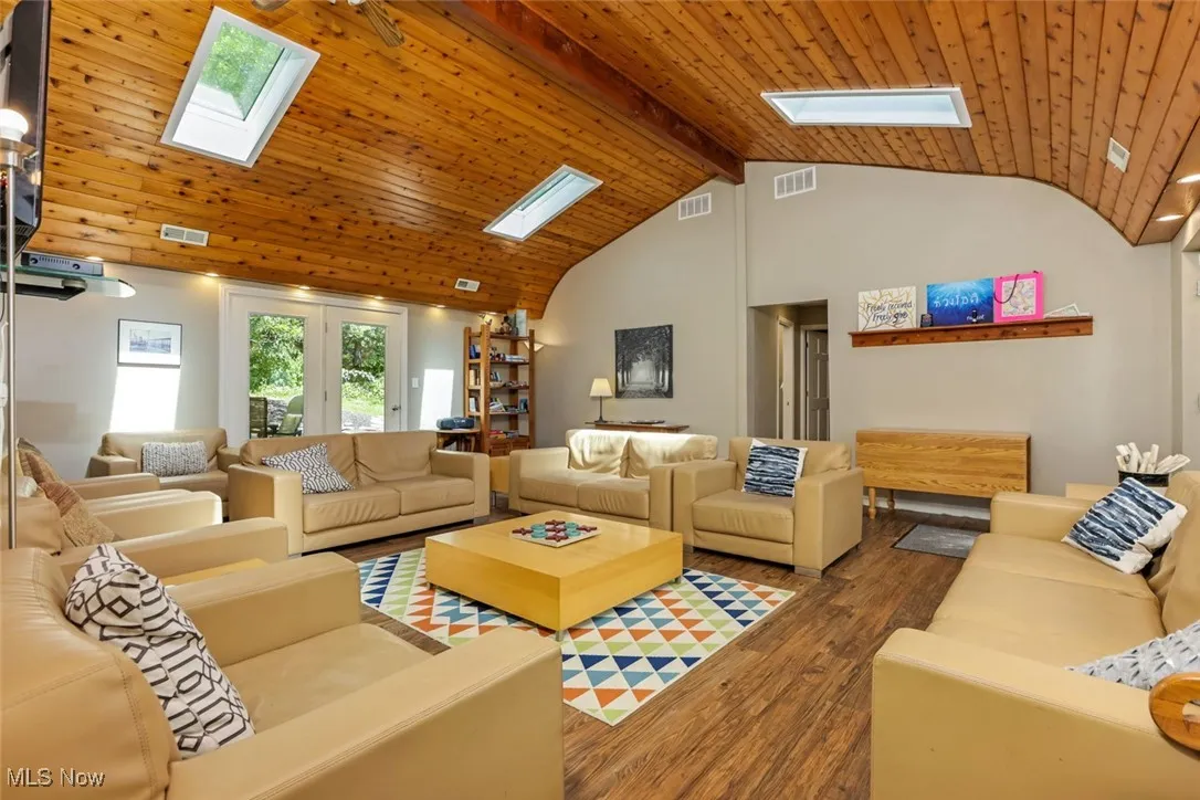 Living room with a skylight, a wood ceiling with exposed beams, wood finished floors, and high vaulted ceiling