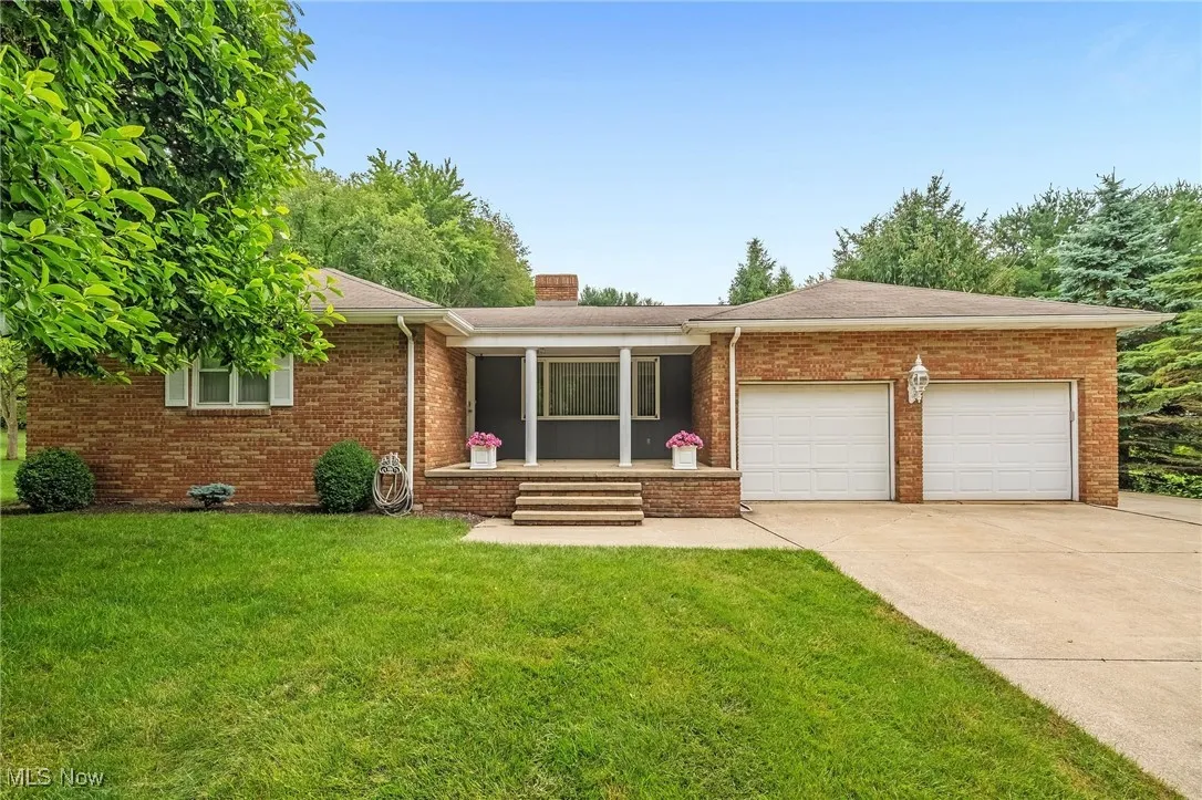 Ranch-style home featuring a garage, concrete driveway, a front lawn, covered porch, and brick siding