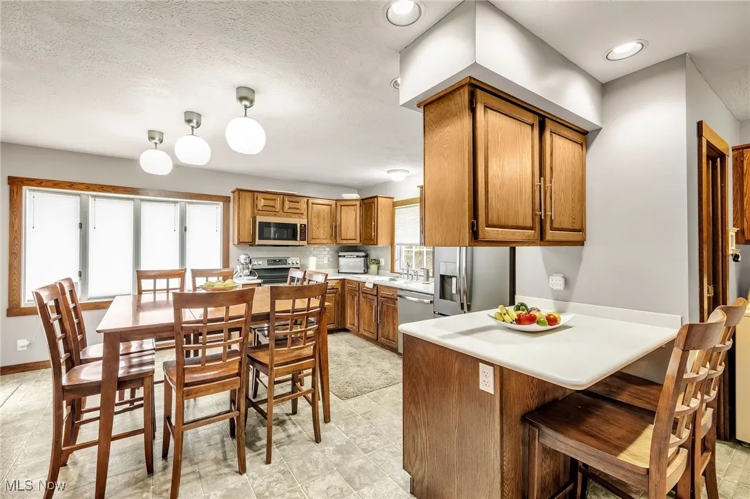 Kitchen featuring appliances with stainless steel finishes, brown cabinets, a peninsula, a kitchen breakfast bar, and light countertops