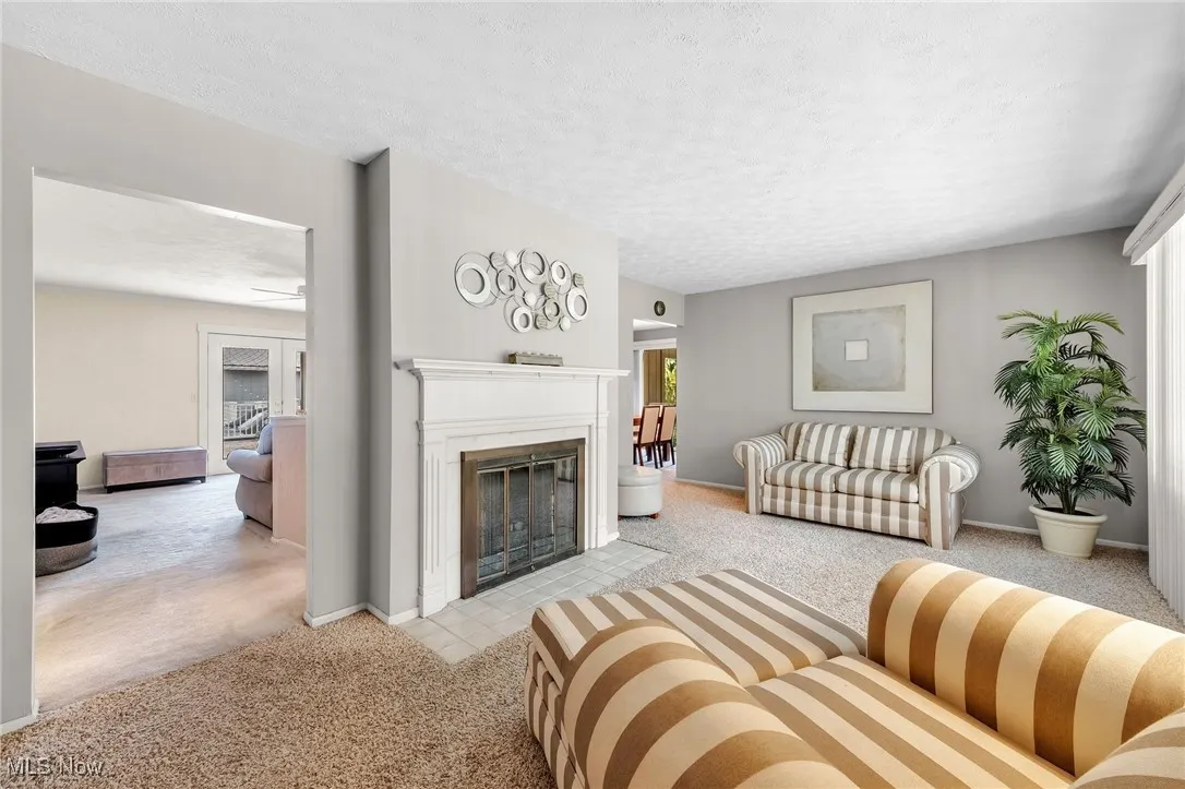 Living room featuring light colored carpet, a textured ceiling, a fireplace with flush hearth, and a ceiling fan