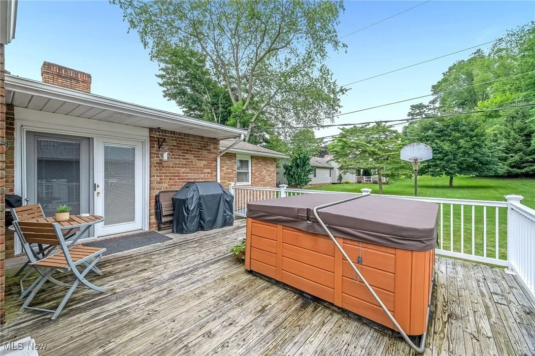 Wooden deck with a hot tub, grilling area, and a lawn