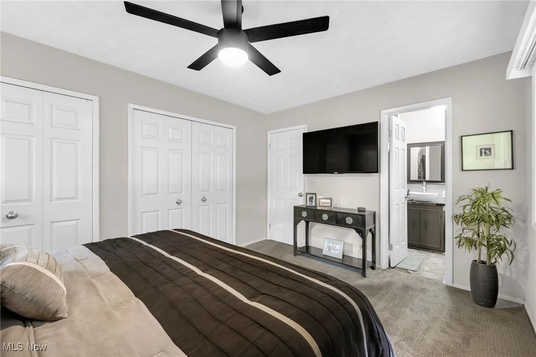 Carpeted bedroom featuring two closets, ensuite bathroom, and ceiling fan