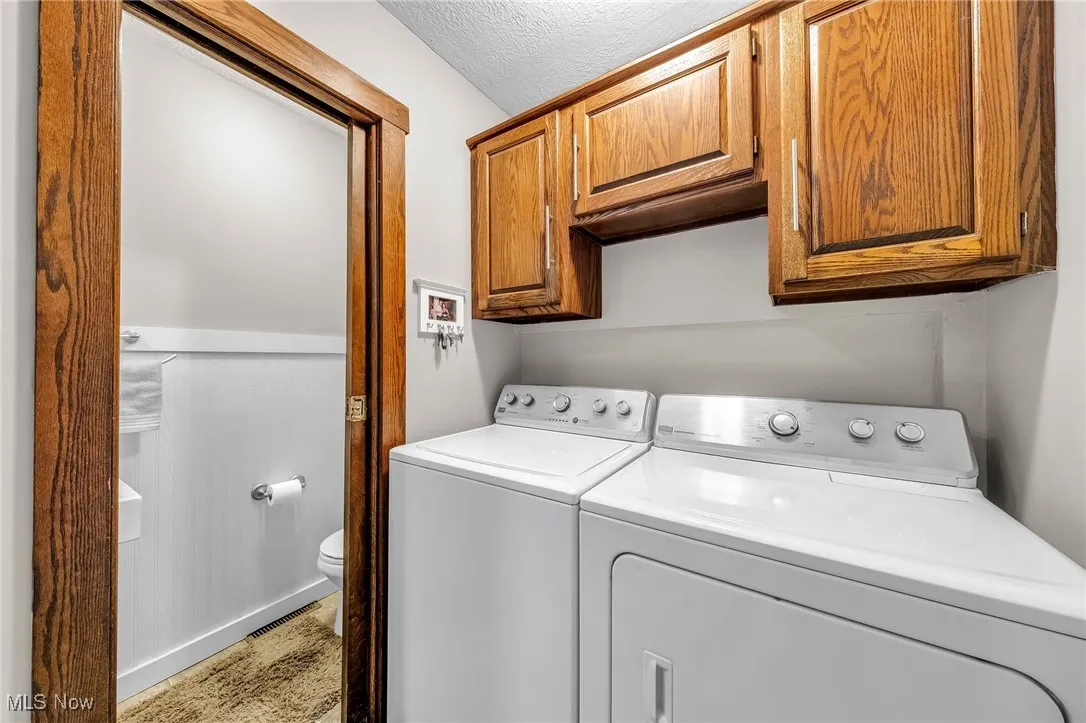 Washroom featuring independent washer and dryer, cabinet space, and a textured ceiling