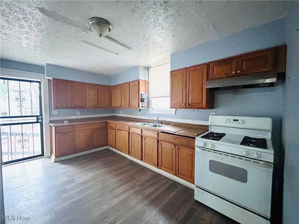 Kitchen featuring dark wood-type flooring, gas range gas stove, under cabinet range hood, a sink, and brown cabinets