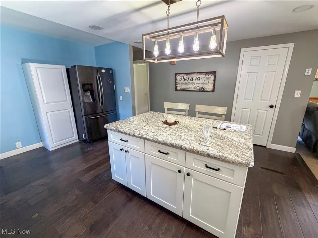 Kitchen featuring decorative light fixtures, white cabinetry, stainless steel refrigerator with ice dispenser, light stone counters, and a center island