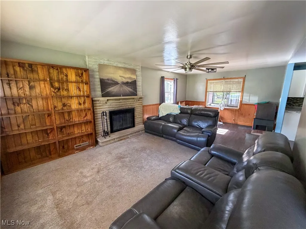 Carpeted living area with a fireplace, ceiling fan, wainscoting, and wood walls