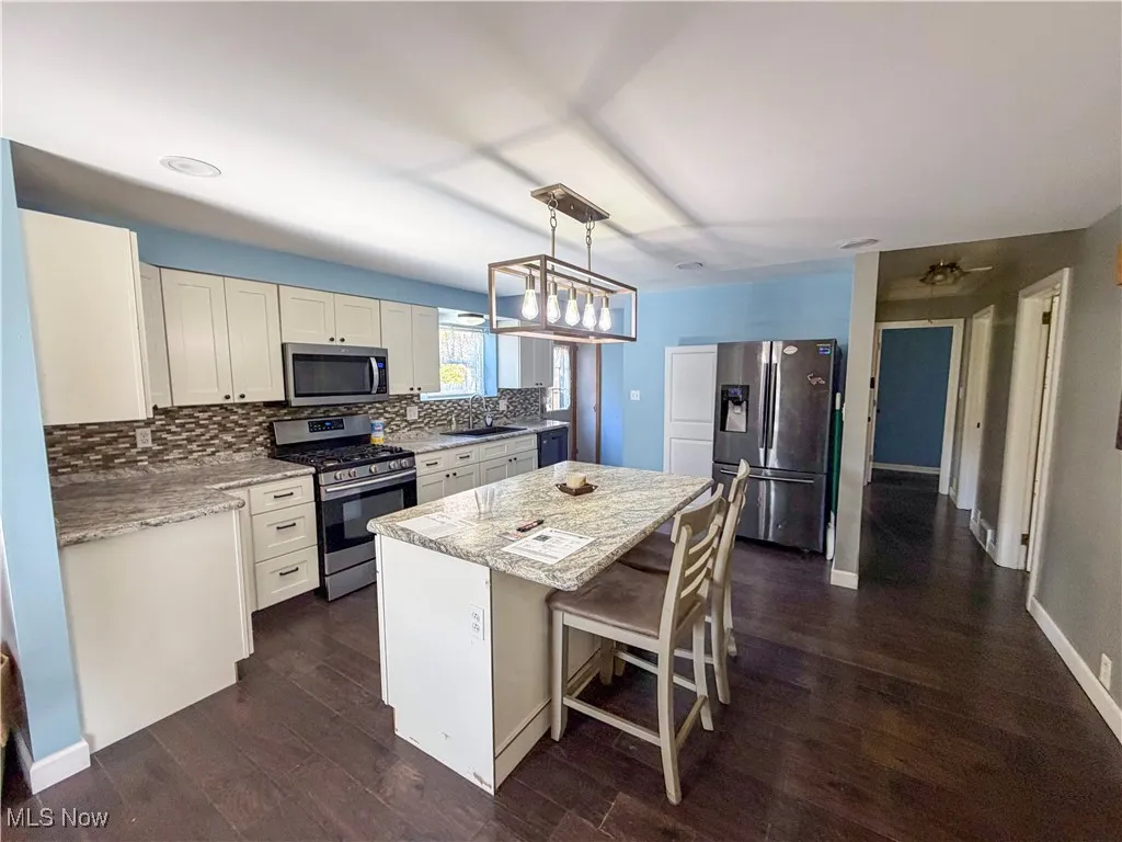 Kitchen featuring stainless steel appliances, white cabinetry, backsplash, light stone counters, and a kitchen breakfast bar