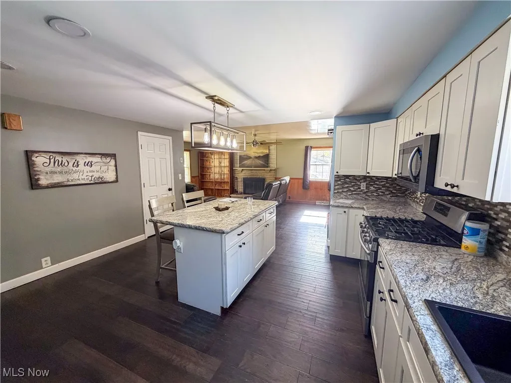 Kitchen with a kitchen bar, white cabinets, pendant lighting, appliances with stainless steel finishes, and light stone counters