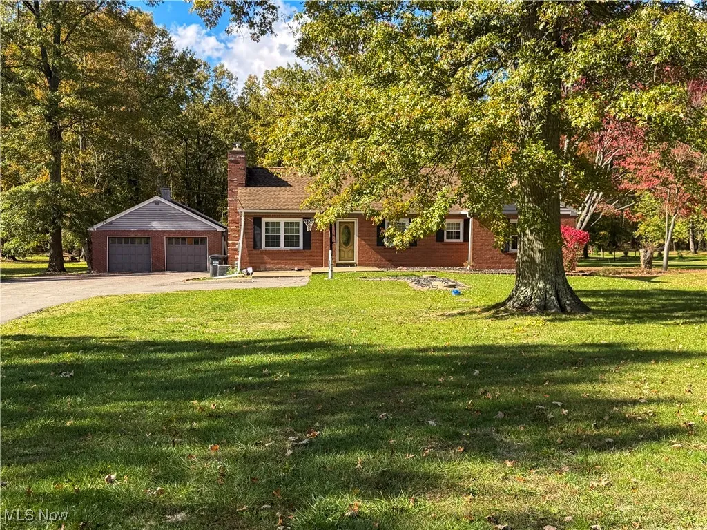 View of front of house featuring a front yard, a chimney, brick siding, and view of scattered trees