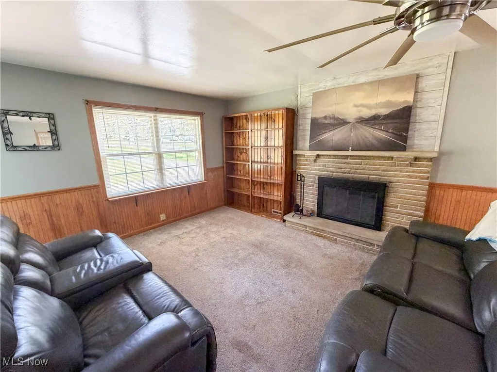Carpeted living room featuring wainscoting, wood walls, a large fireplace, and ceiling fan