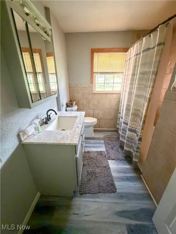 Bathroom with tile walls, a shower with shower curtain, vanity, dark wood-style flooring, and a wainscoted wall