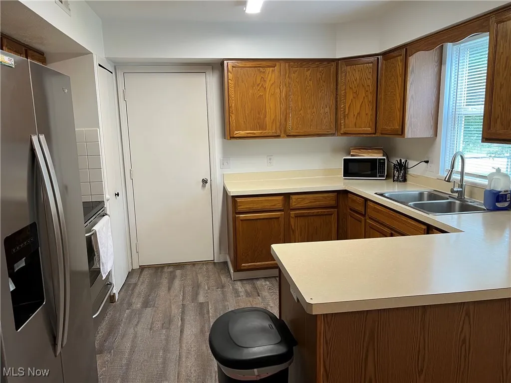 Kitchen featuring stainless steel refrigerator with ice dispenser, black microwave, wood finished floors, and light countertops