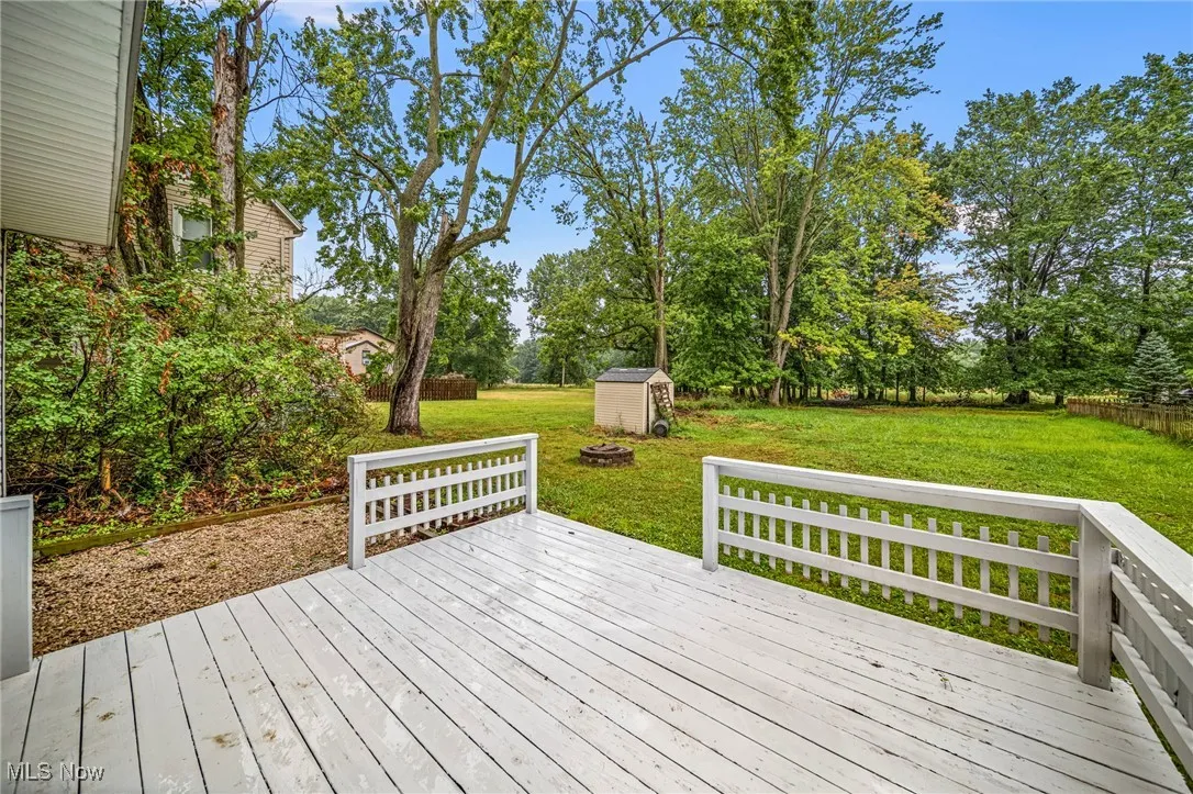 Wooden deck with a shed, a lawn, and view of wooded area