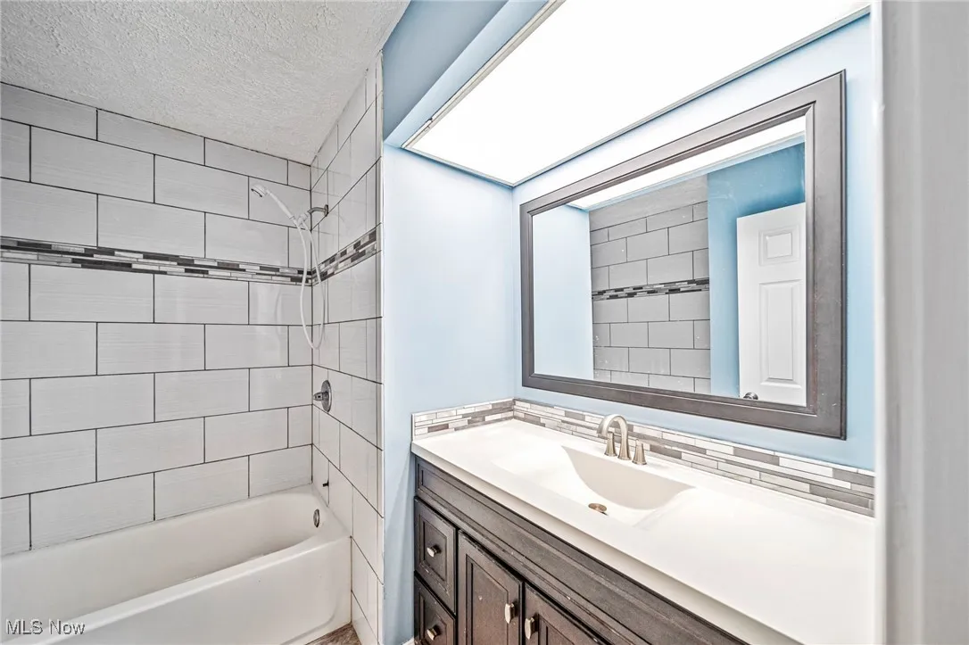 Bathroom featuring vanity, bathtub / shower combination, and a textured ceiling