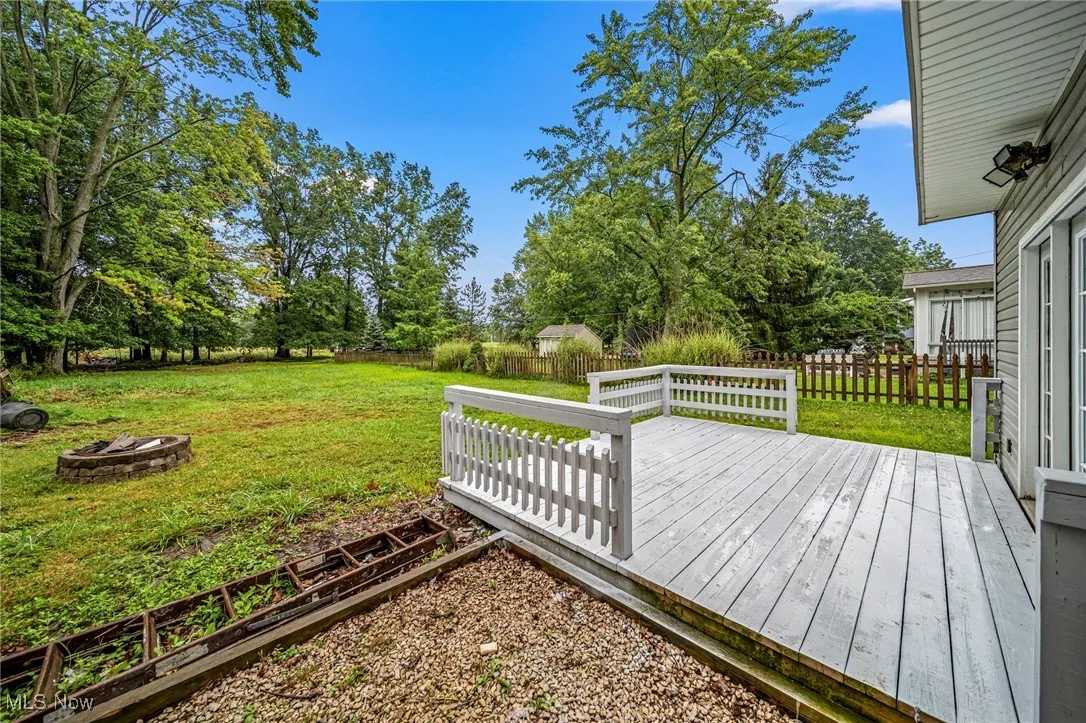 Wooden deck with an outdoor fire pit, a fenced backyard, and view of wooded area