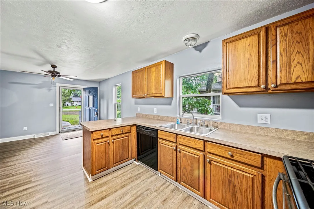 Kitchen with brown cabinetry, a peninsula, a textured ceiling, range, and light countertops
