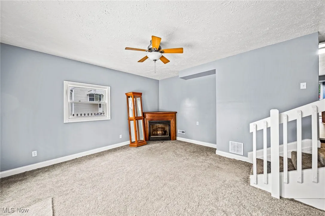 Unfurnished living room with carpet, a textured ceiling, a fireplace, and ceiling fan